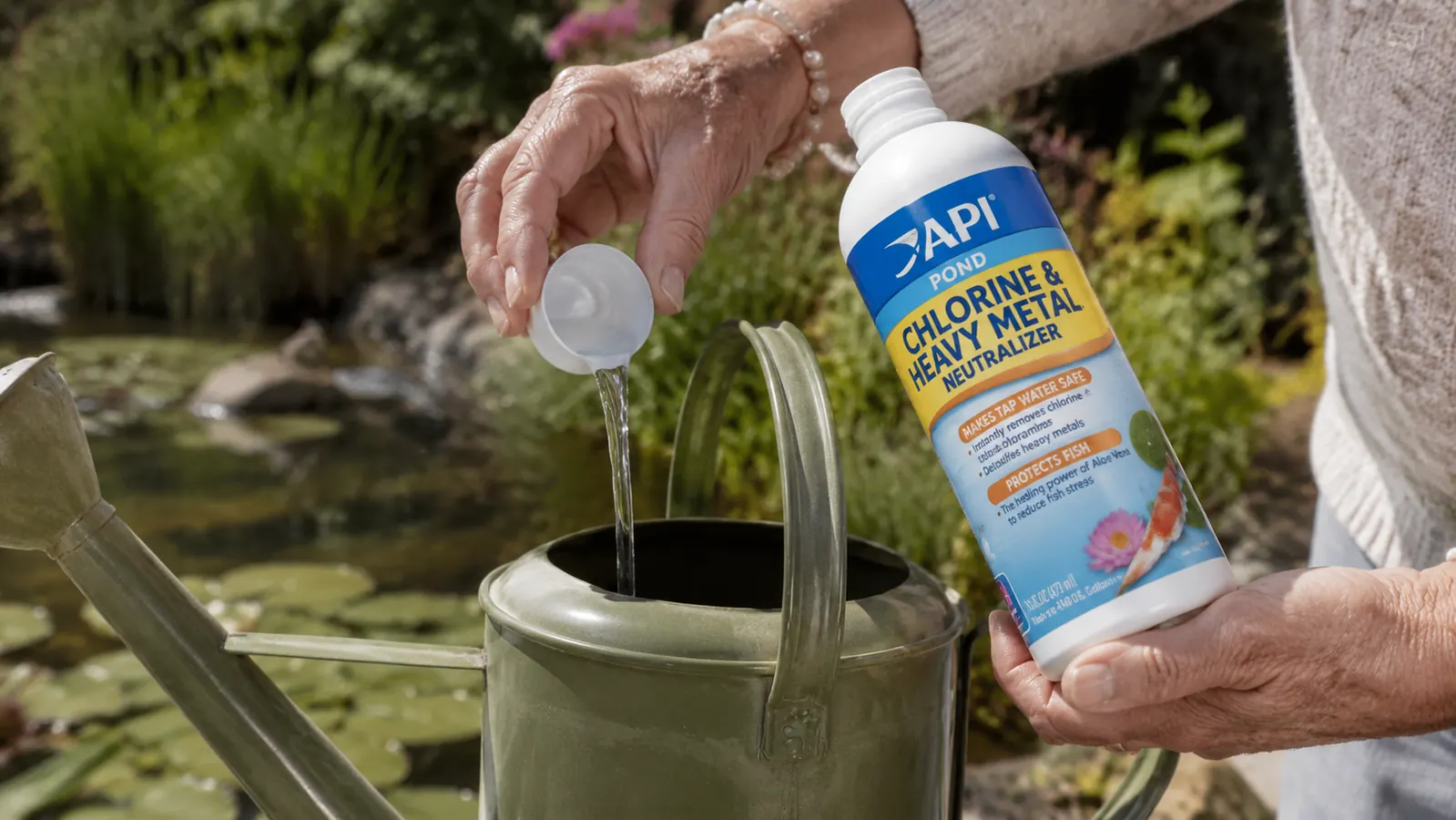 Hand measuring and pouring API Pond Chlorine Neutralizer into a watering can beside a garden pond