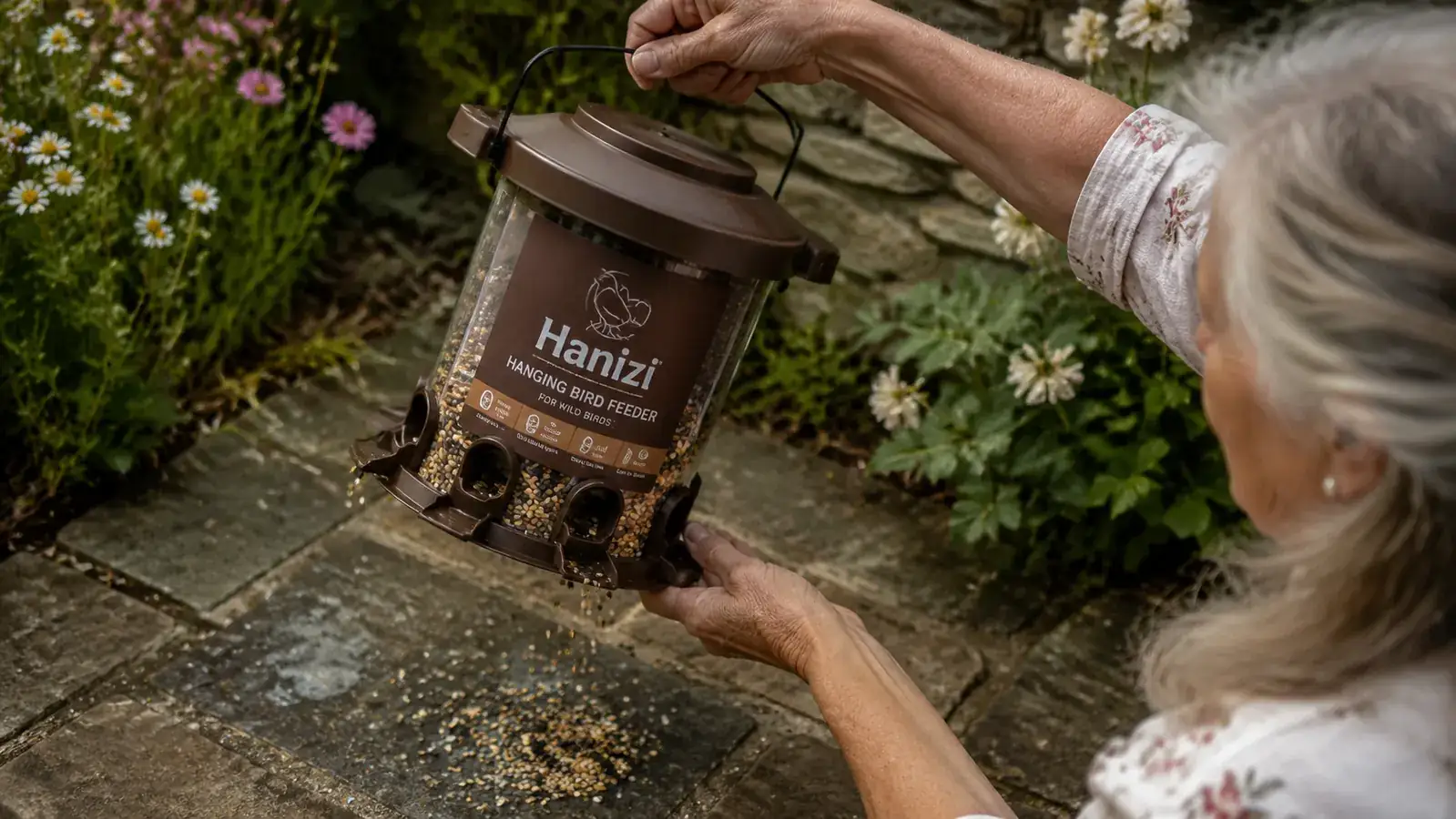Close-up of seeds scattered on a stone paving slab beneath a hanging bird feeder, showing seed waste on the ground