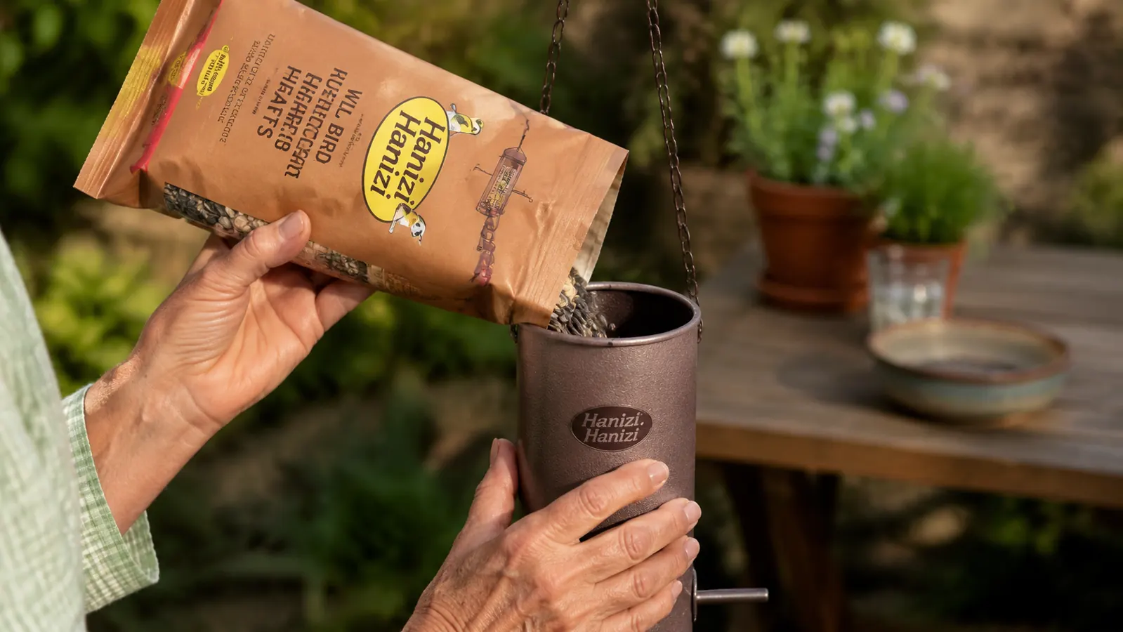 Hands filling the Hanizi bird feeder with sunflower seeds over a garden table